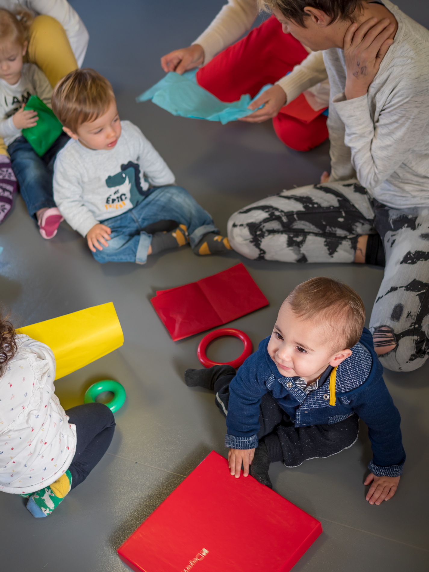 Des enfants et leurs accompagnants jouent au sol avec des objets colorés