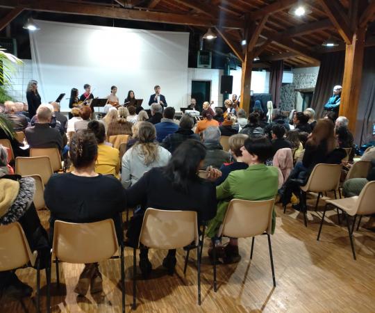Des dizaines de personnes assistent, assis, aux vœux du maire de Vienne dans la salle de réception du centre social Malissol; un orchestre est sur scène avec lui